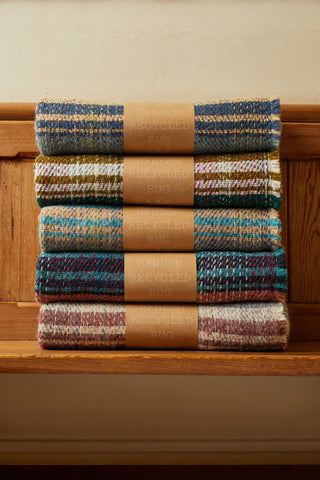 Stacked small checked random recycled wool blankets with colorful blue green and earth tone stripes handcrafted from recycled wool