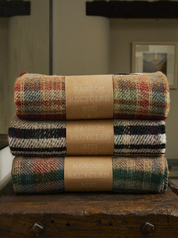 Stacked small checked random recycled wool blankets in warm earthy tones with textured woven fabric