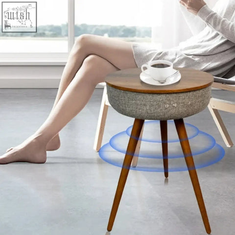 A modern smart coffee table with a wooden top, gray fabric base, tapered legs, and built-in speakers