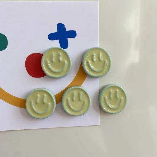 Five pale green ceramic smiley face magnets with a glossy finish in a smiling glow fridge magnet pack