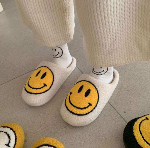 Cream-colored smiling slippers with bright yellow smiley face made of soft faux fur for cozy indoor wear