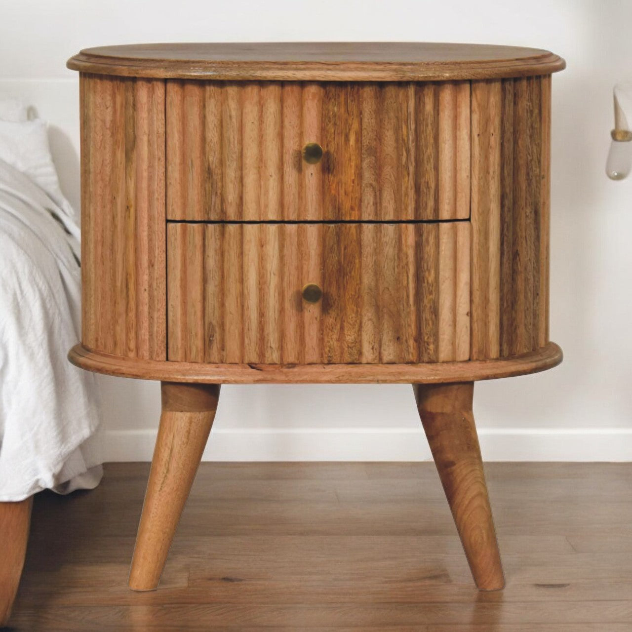 A rustic oval nightstand with vertical wood slats and brass knobs made from oak mango wood perfect for bedside use