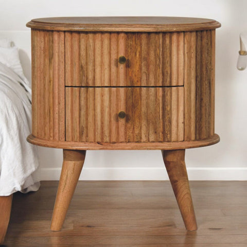 A rustic oval nightstand with vertical wood slats and brass knobs made from oak mango wood perfect for bedside use