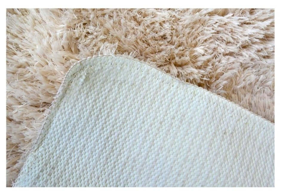 Back side of a soft washable beige shaggy rug with light blue woven backing and tightly stitched edge