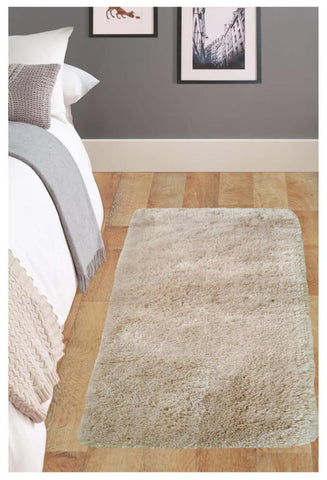 A soft washable beige shaggy rug with a plush textured surface lies on a wooden floor beside a bed