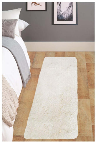 A soft washable ivory shaggy rug with plush texture lies on the wooden floor beside a bed
