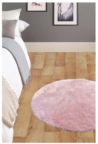 A soft washable pink shaggy rug with a plush round shape and cozy texture on a wooden floor