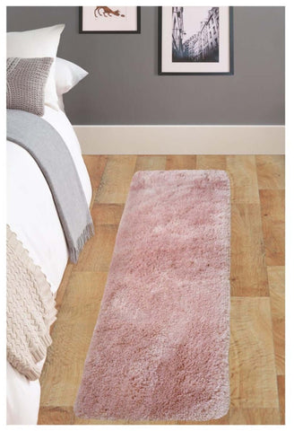 A soft washable pink shaggy rug with plush fluffy texture lies on wooden floor beside the bed