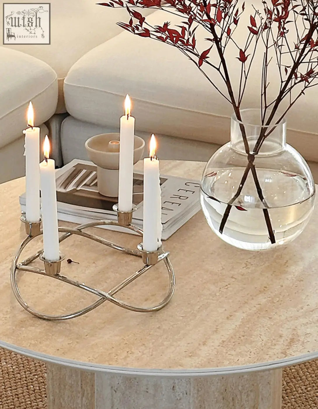 Silver metallic candle holder with elegant intertwined design holding four lit white candles on solveig marble round coffee table