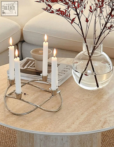 Silver metallic candle holder with elegant intertwined design holding four lit white candles on solveig marble round coffee table