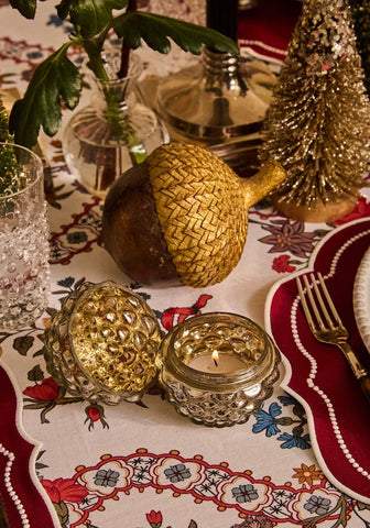 Golden intricately woven acorn centerpiece with dark brown base and metallic gold cap on sommerset scroll red cotton tablecloth
