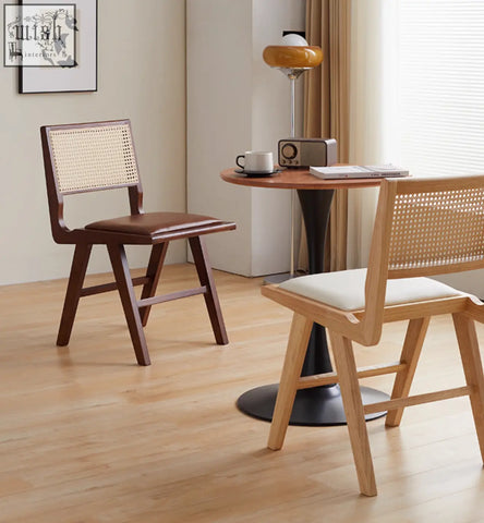 A pair of sophia rattan dining chairs with one dark wood and brown leather seat and one light wood with white cushion