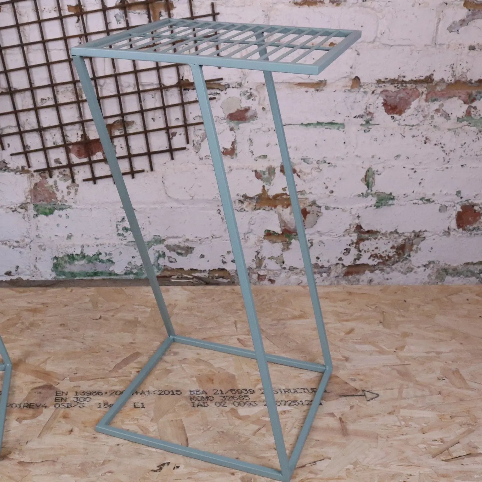 A light blue metal plant stand with a rectangular grid top and angled legs perfect for a green garden table set