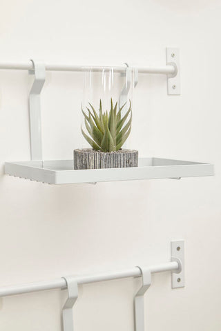 White iron single shelf storage rack by sorello with a white metal shelf and a green succulent in a glass dome