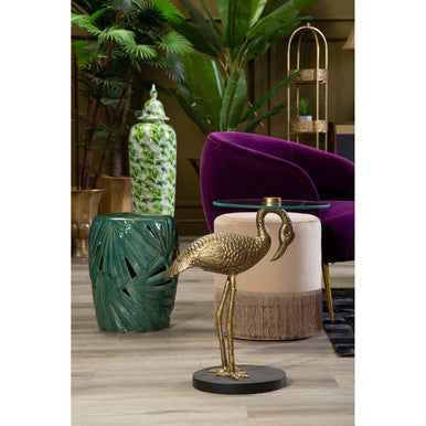 Golden flamingo statue with intricate detailing on a black base displayed on a sorrell green ceramic table