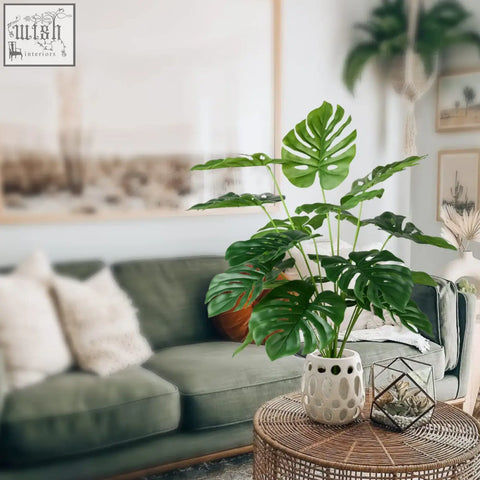 A white ceramic planter with textured holes holding a vibrant green fake tropical palm tree monstera plant