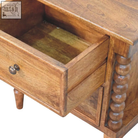 Warm-toned amber oak bedside table with a single drawer and turned spindle legs featuring a round brass knob