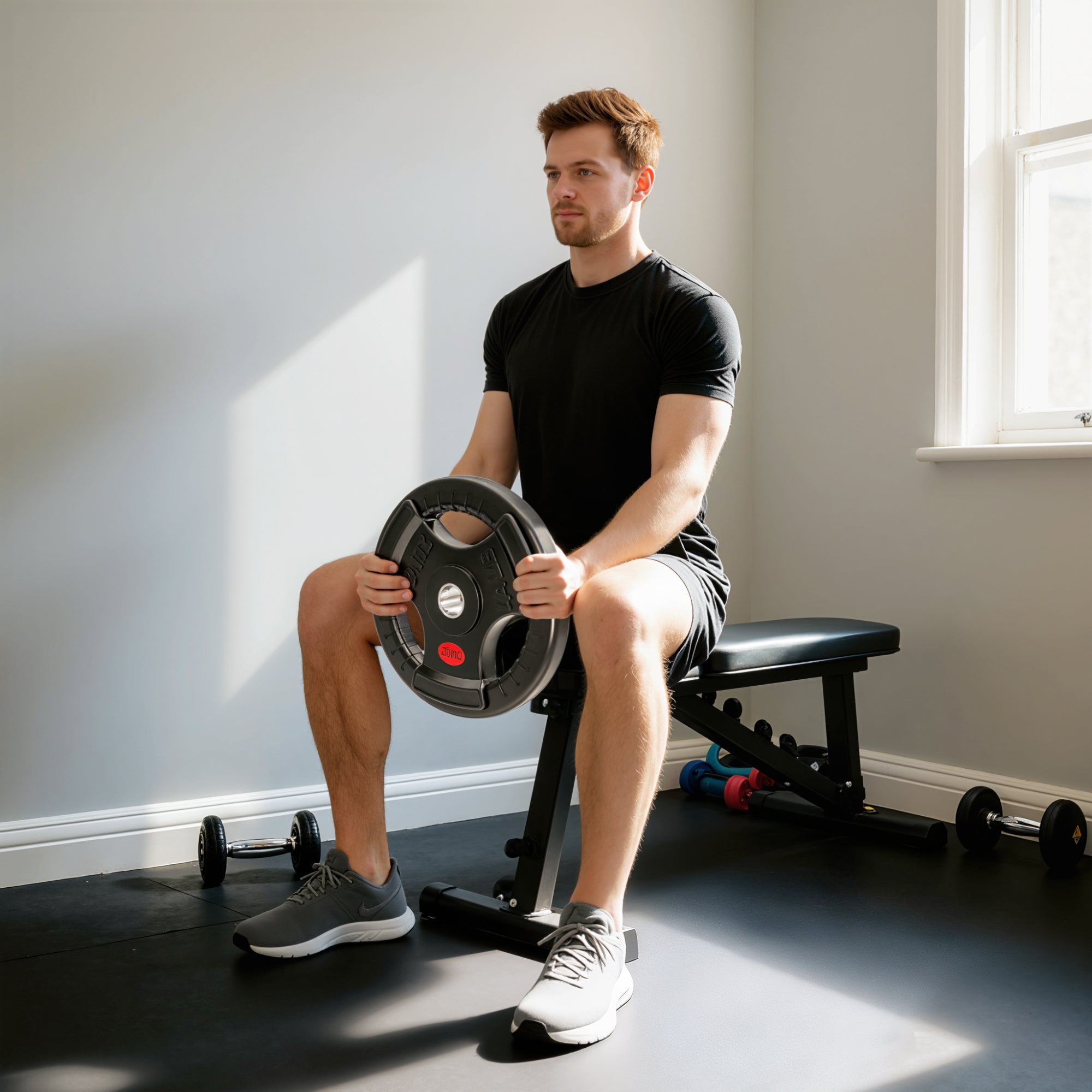 Man seated on bench holding black sportnow olympic weight plate with red and silver logo for strength training