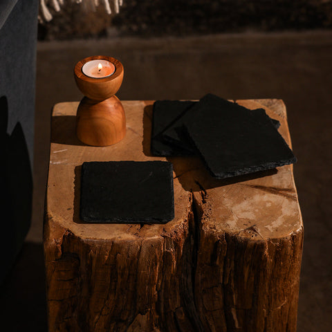 Square slate coasters set of 4 in black slate resting on a wooden stump next to a warm-toned wooden candle holder gift box