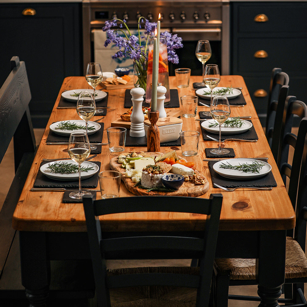 Wooden dining table set with dark blue cabinets and black chairs featuring square slate coasters in gift box centerpiece