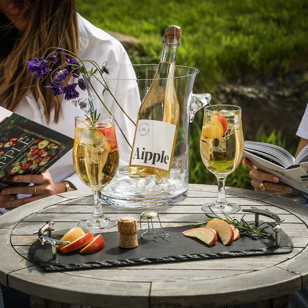 A clear glass ice bucket holding a bottle of apple sparkling cider with stag craft beer glasses set of 2 nearby