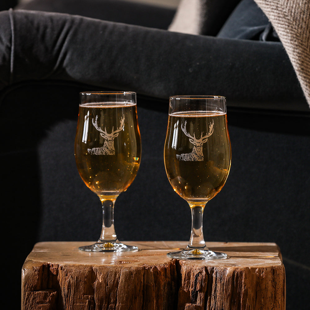 Two clear glass stag craft beer glasses featuring white etched stag design filled with golden bubbly craft beer