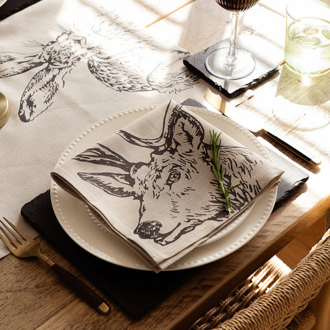 Beige linen napkin with black fox face illustration folded on white plate from stag linen napkins set of 2