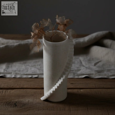 A minimalist white ceramic vase from the stairs series with wavy sculpted detail holding dried brown flowers 4am product design