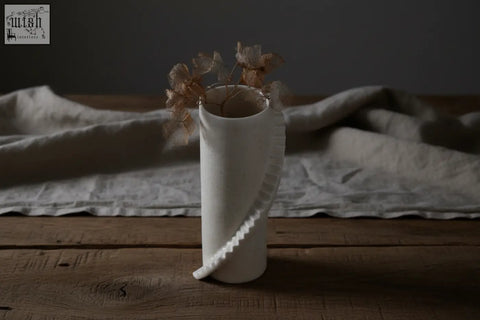 White ceramic vase from stairs series by 4am product design with wavy sculpted detail and dried beige flowers inside