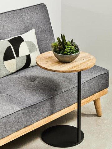 Round wooden side table with black metal base and small potted succulent next to stockholm 3 seat grey sofa bed