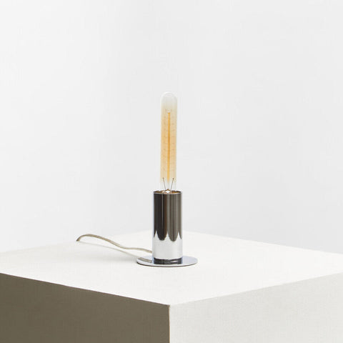 A sleek stockholm chrome finish table lamp with a cylindrical chrome finish base and warm glowing edison bulb