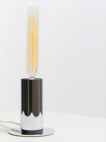 A stockholm chrome finish table lamp with a sleek cylindrical chrome finish base and a clear glass edison bulb