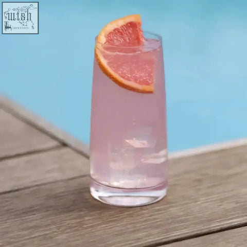 A tall clear stolzle experience highball glass filled with pink soft drink and ice cubes garnished with grapefruit slice