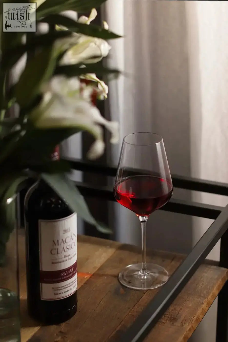 A clear stemmed stolzle lausitz quatrophil red wine glass filled with red wine beside a macan classic bottle on wood