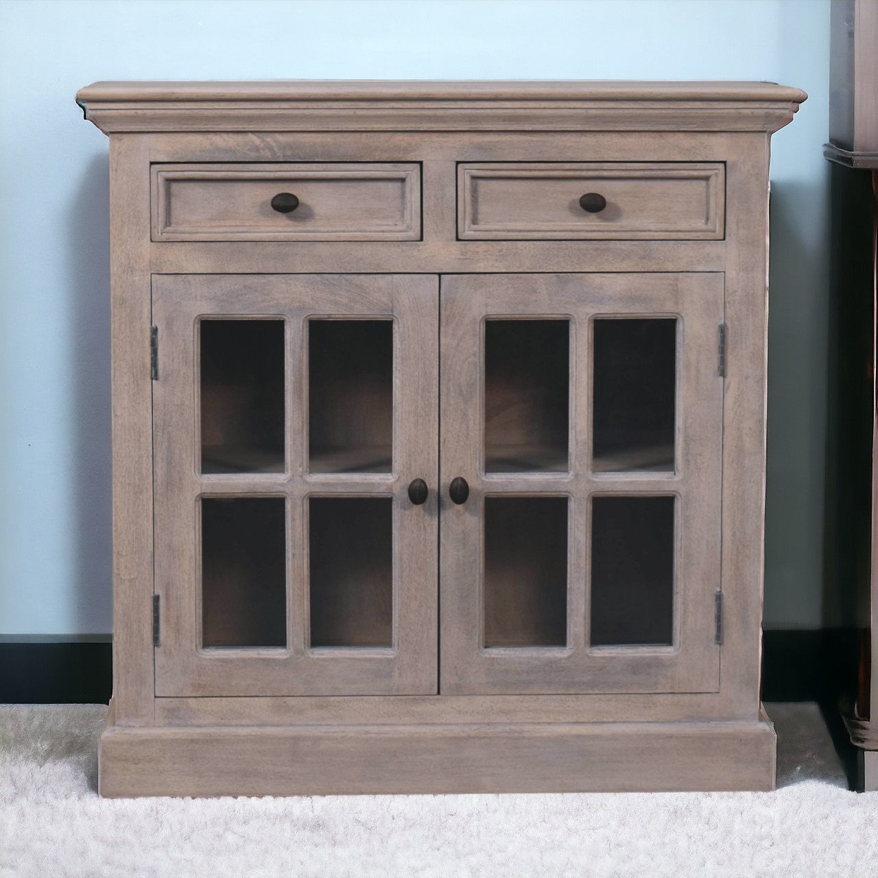 A rustic gray stone finish cabinet with glazed doors and two drawers featuring dark round knobs