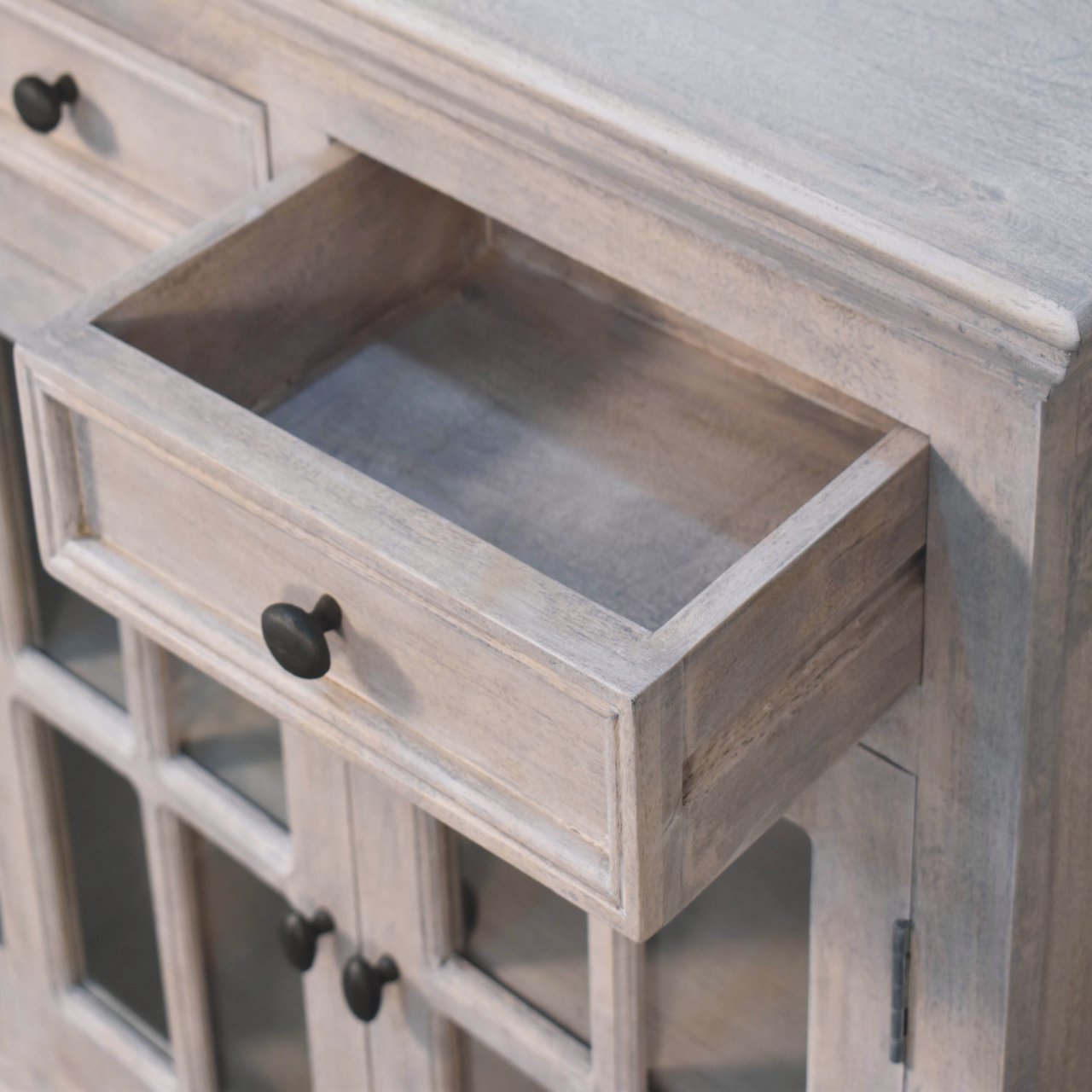 A rustic light gray wooden stone finish cabinet with black knobs and glazed doors for stylish storage