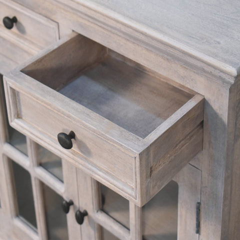 A rustic light gray wooden stone finish cabinet with black knobs and glazed doors for stylish storage