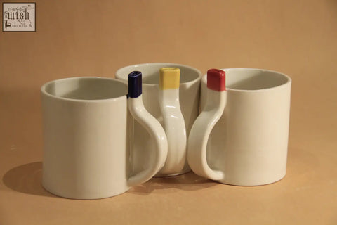 Three white ceramic straw cup mugs with uniquely shaped handles and blue yellow and red colored caps