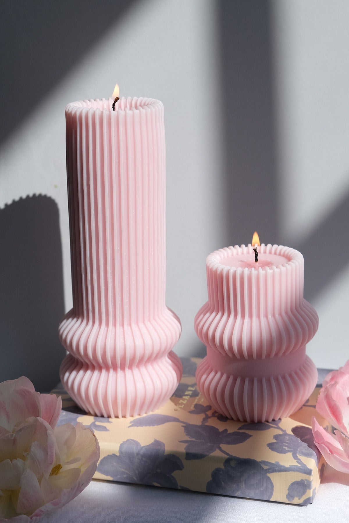 Two lit pale pink striped pillar candles with vertical ribbed texture and fluted bases for home decor