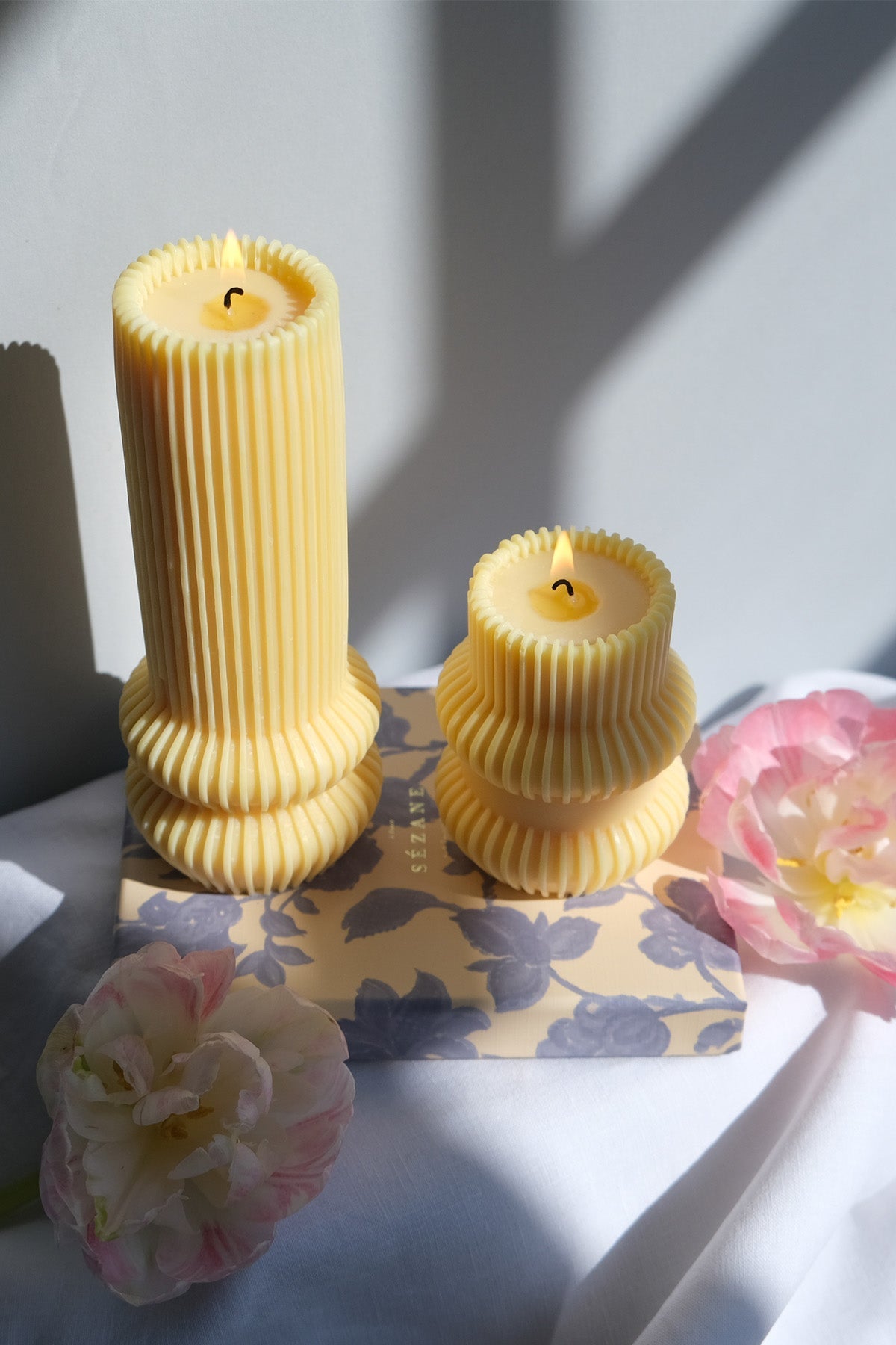 Two pale yellow striped pillar candles with vertical ribbing and tiered base design for home decor
