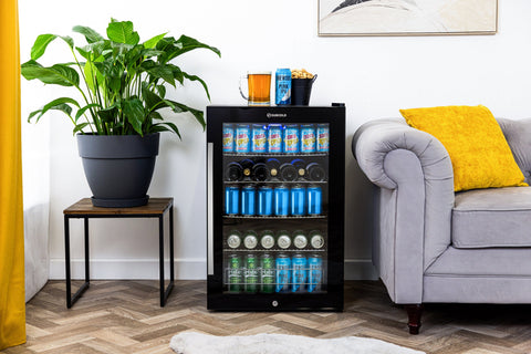 Black subcold ace130 beer fridge with glass door, multiple shelves of canned drinks, and top shelf with mug and popcorn bucket