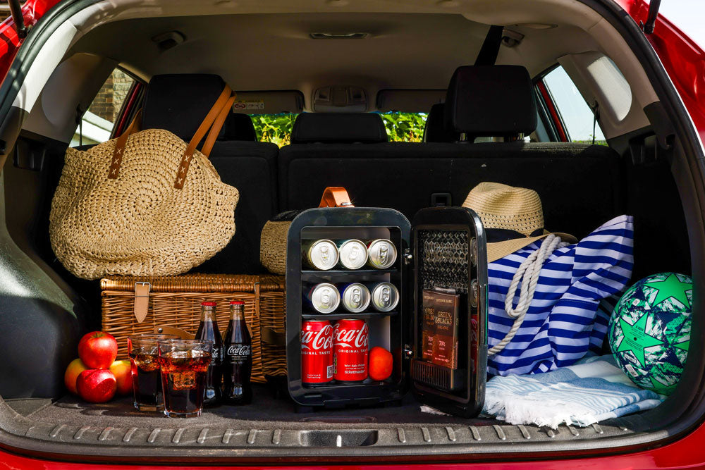 Black Subcold Pro 10l mini fridge with glass doors and silver handles stocked with coca-cola cans and chocolate bars