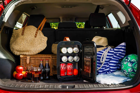 Black Subcold Pro 10l mini fridge with glass doors and silver handles stocked with coca-cola cans and chocolate bars