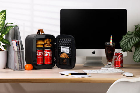 Black subcold pro 4l mini fridge with brown leather handle and interior shelves holding canned drinks and snacks