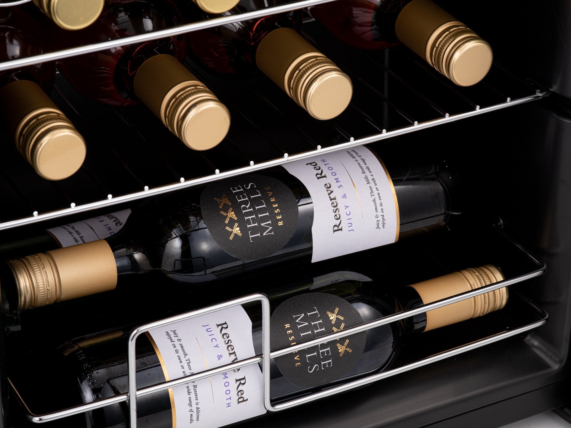 Black glass wine bottles with gold foil caps labeled three mills reserve red in a stainless steel rack inside the subcold viva24 led wine cooler