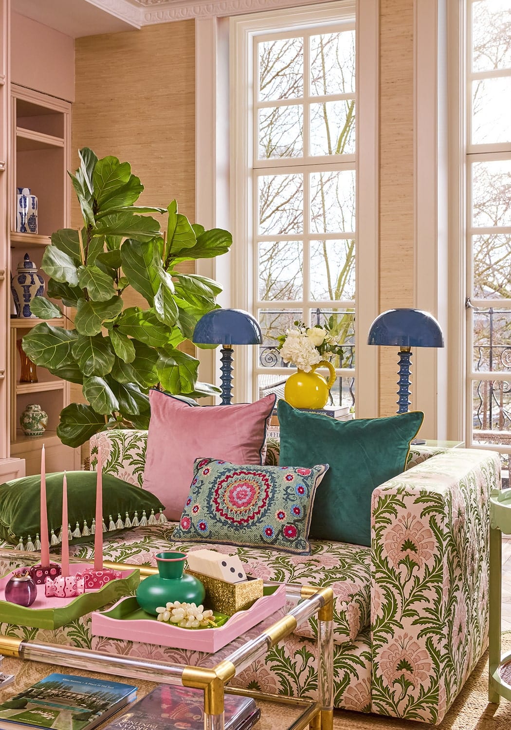 A plush sofa with vibrant pink and green floral fabric and matching pillows next to a handcrafted yellow jug