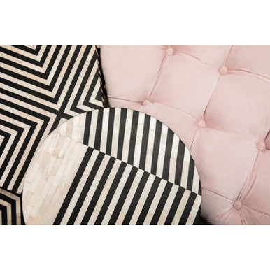 A round black-and-white striped table with geometric pattern beside a tufted pink blossom fabric chesterfield sofa
