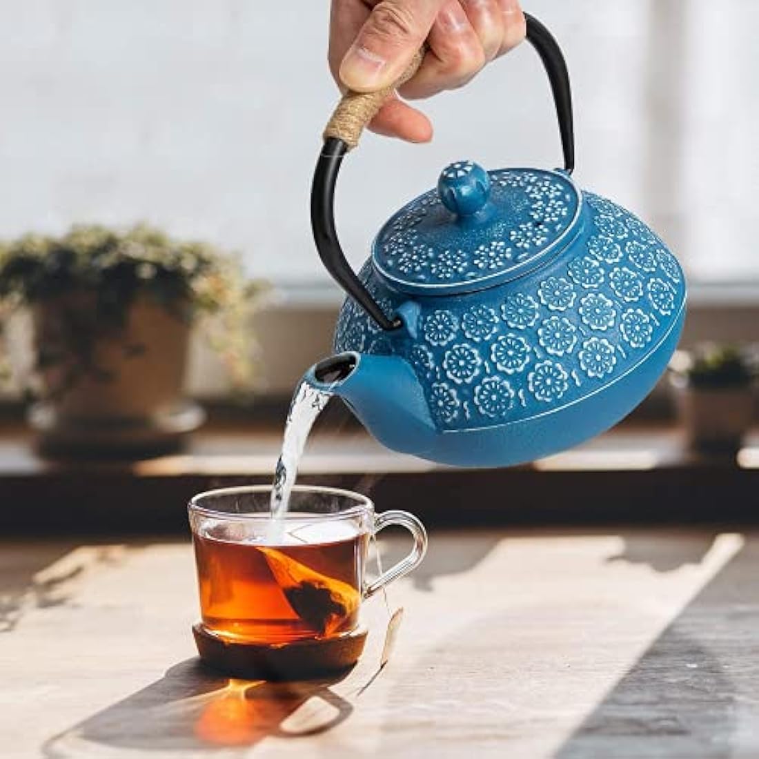 A vibrant blue cast iron teapot with white floral patterns black handle and spout perfect for loose leaf tea brewing