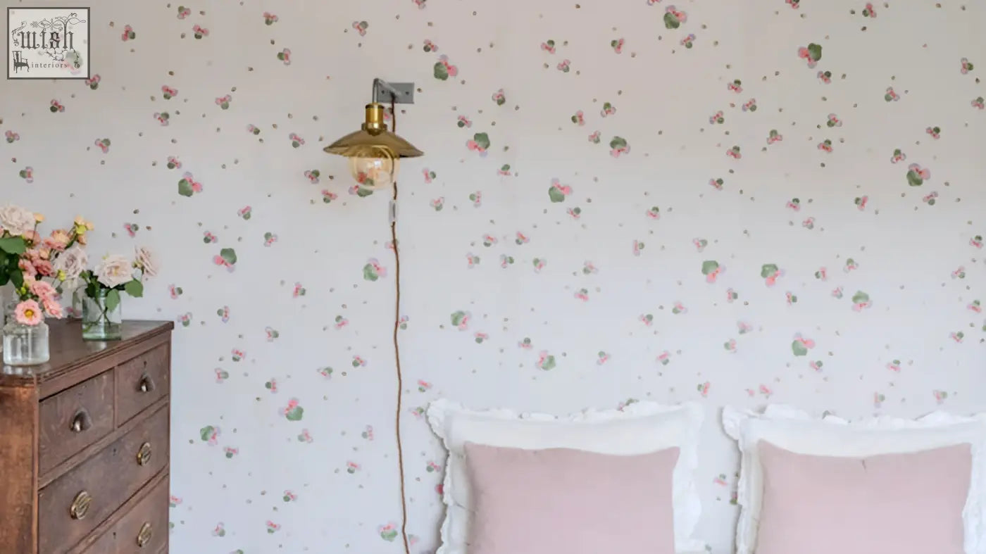 A brass wall-mounted lamp with vintage bell-shaped shade and exposed filament bulb in sweet clover wallpaper with three leaves