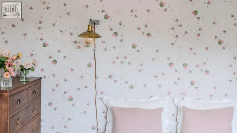 A brass wall-mounted lamp with vintage bell-shaped shade and exposed filament bulb in sweet clover wallpaper with three leaves